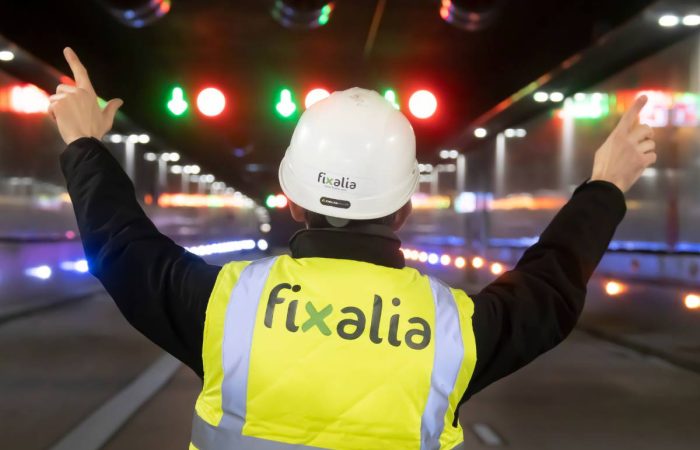 Técnico de Fixalia con casco y chaleco reflectante supervisando paneles de mensaje variable LED en autopista nocturna, destacando su liderazgo en soluciones de señalización vial inteligente y gestión del tráfico.