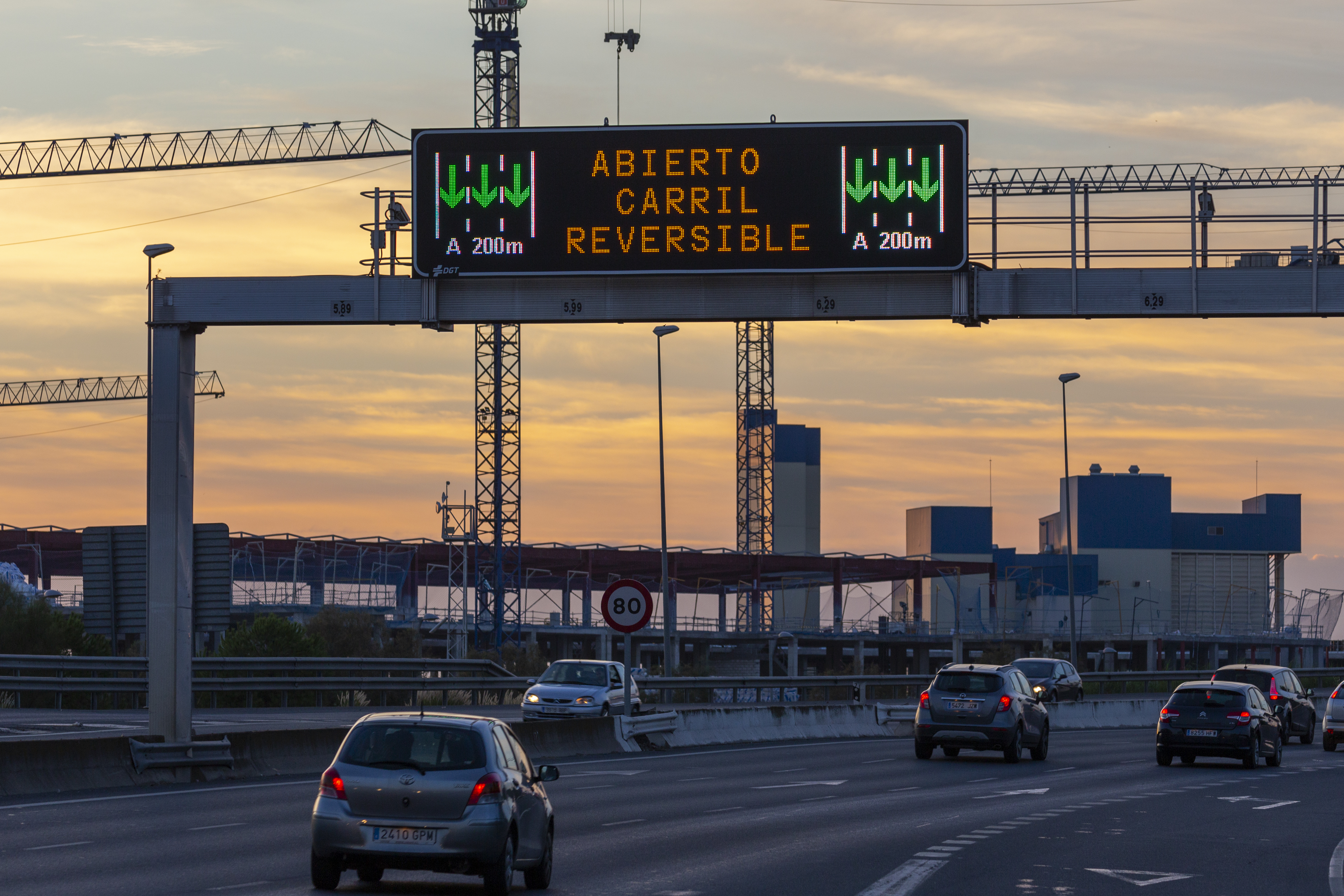 Panel de mensaje variable Full Matrix en una autopista mostrando “Abierto carril reversible”, con flechas verdes y tráfico al atardecer.