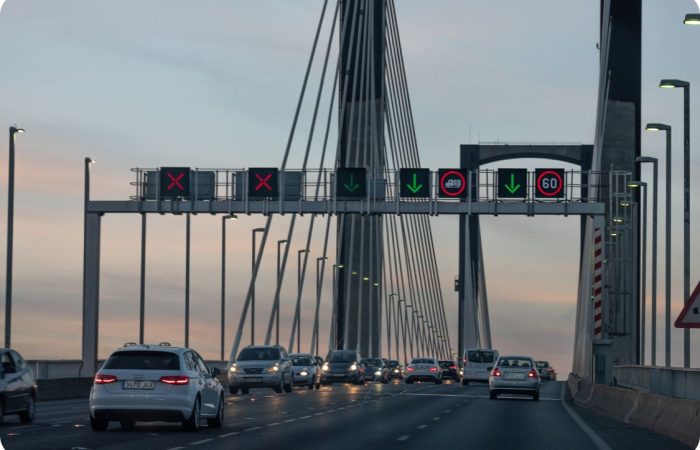Paneles PMV Full Matrix LED instalados en pórtico sobre puente atirantado, mostrando control dinámico de carriles con aspas rojas, flechas verdes y limitación de velocidad variable. Sistema de señalización inteligente para gestión del tráfico en tiempo real, regulación de velocidad y seguridad vial en infraestructuras críticas. Tecnología LED de alta visibilidad desarrollada por Fixalia.