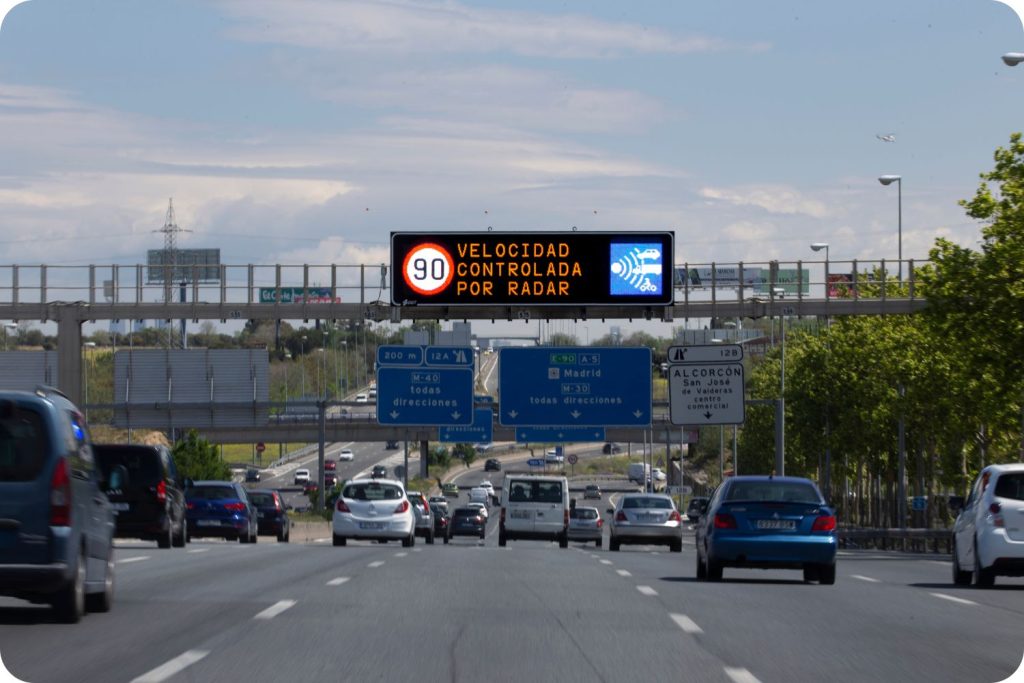 : Panel informativo de tráfico con límite de velocidad de 90 km/h, aviso de velocidad controlada por radar y pictograma luminoso de vigilancia en carretera