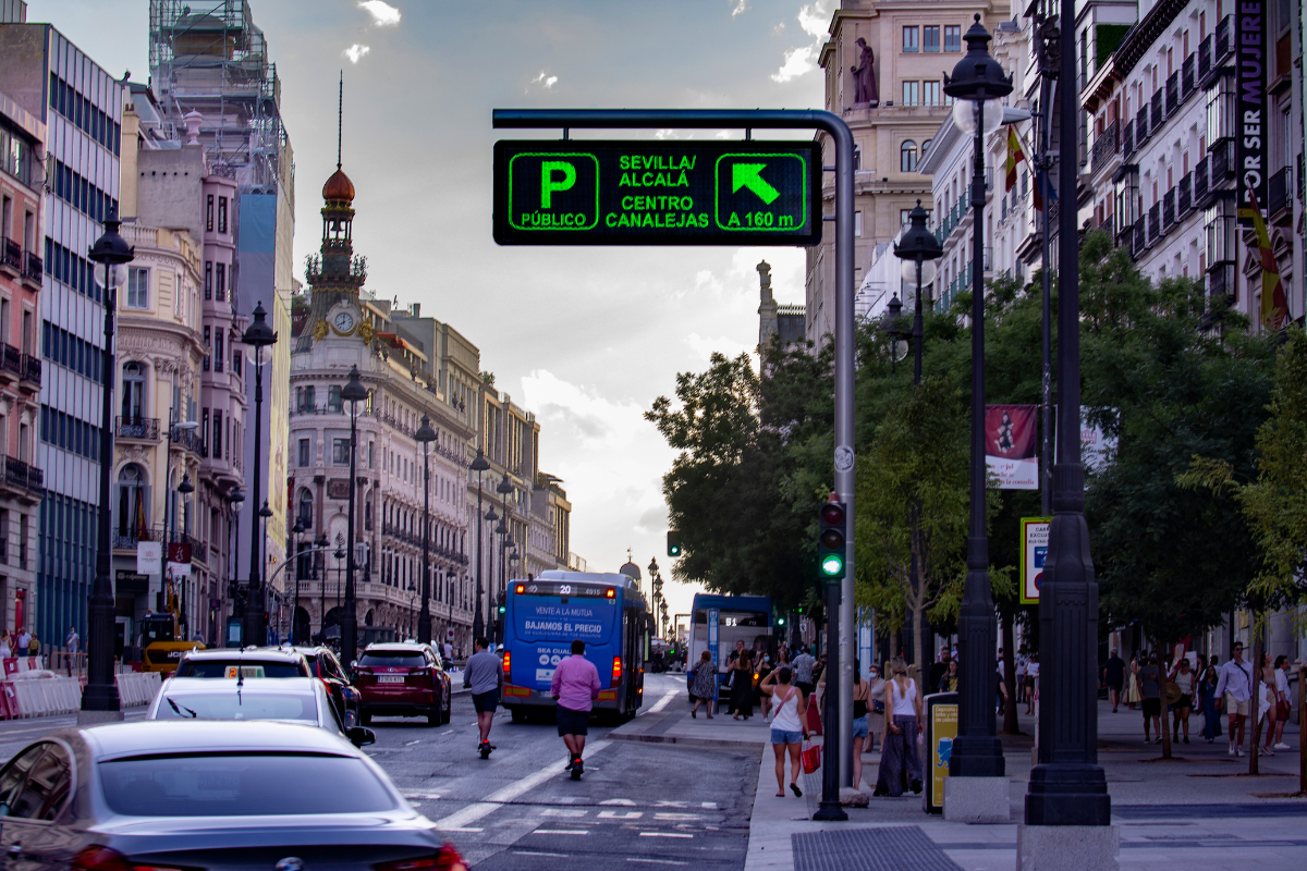 Panel de señalización urbana inteligente con indicación de parking público «Sevilla/Alcalá – Centro Canalejas» a 160 m, instalado sobre una calle del centro de Madrid con tráfico rodado y peatones